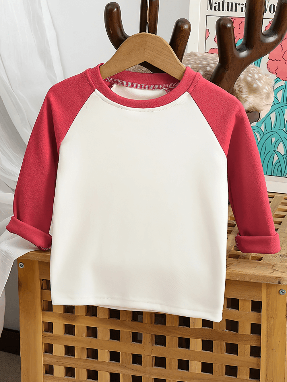 Cute kids top with red raglan sleeves and round neck, displayed on a wooden hanger. Perfect for a playful and comfy look.